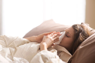 Kranke junge Frau im Bett mit Taschentuch.