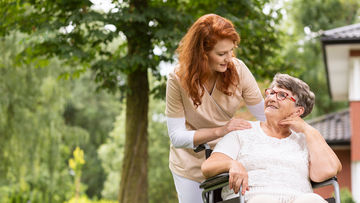 Pflegerin unterhält sich mit Seniorin im Rollstuhl im Park der Seniorenresidenz.