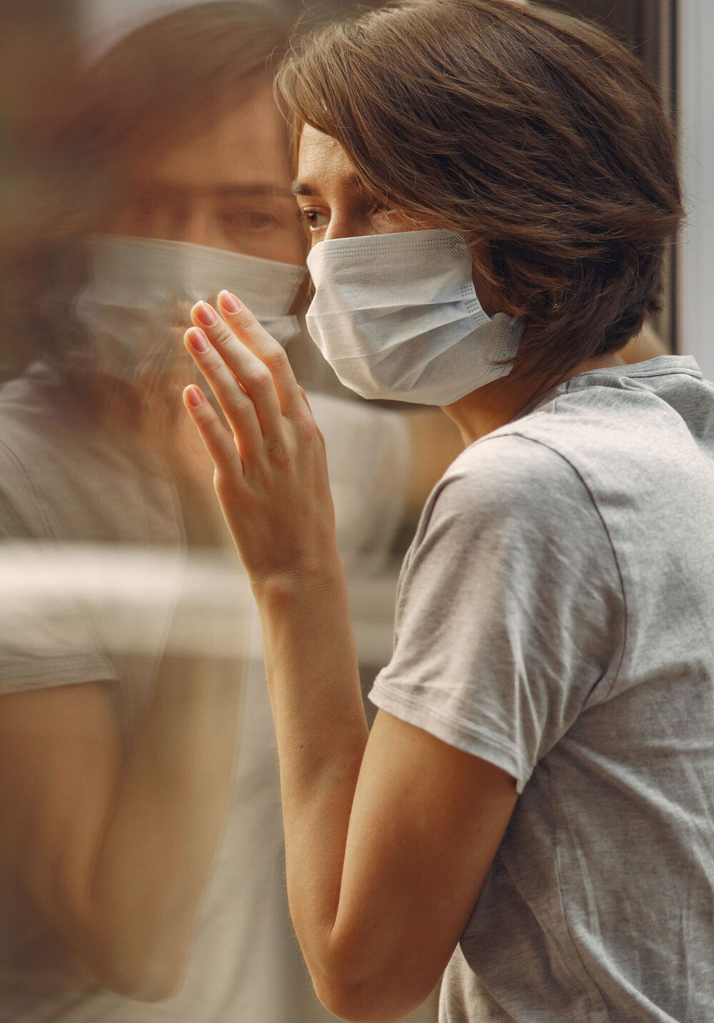 Woman in a mask stands by the window