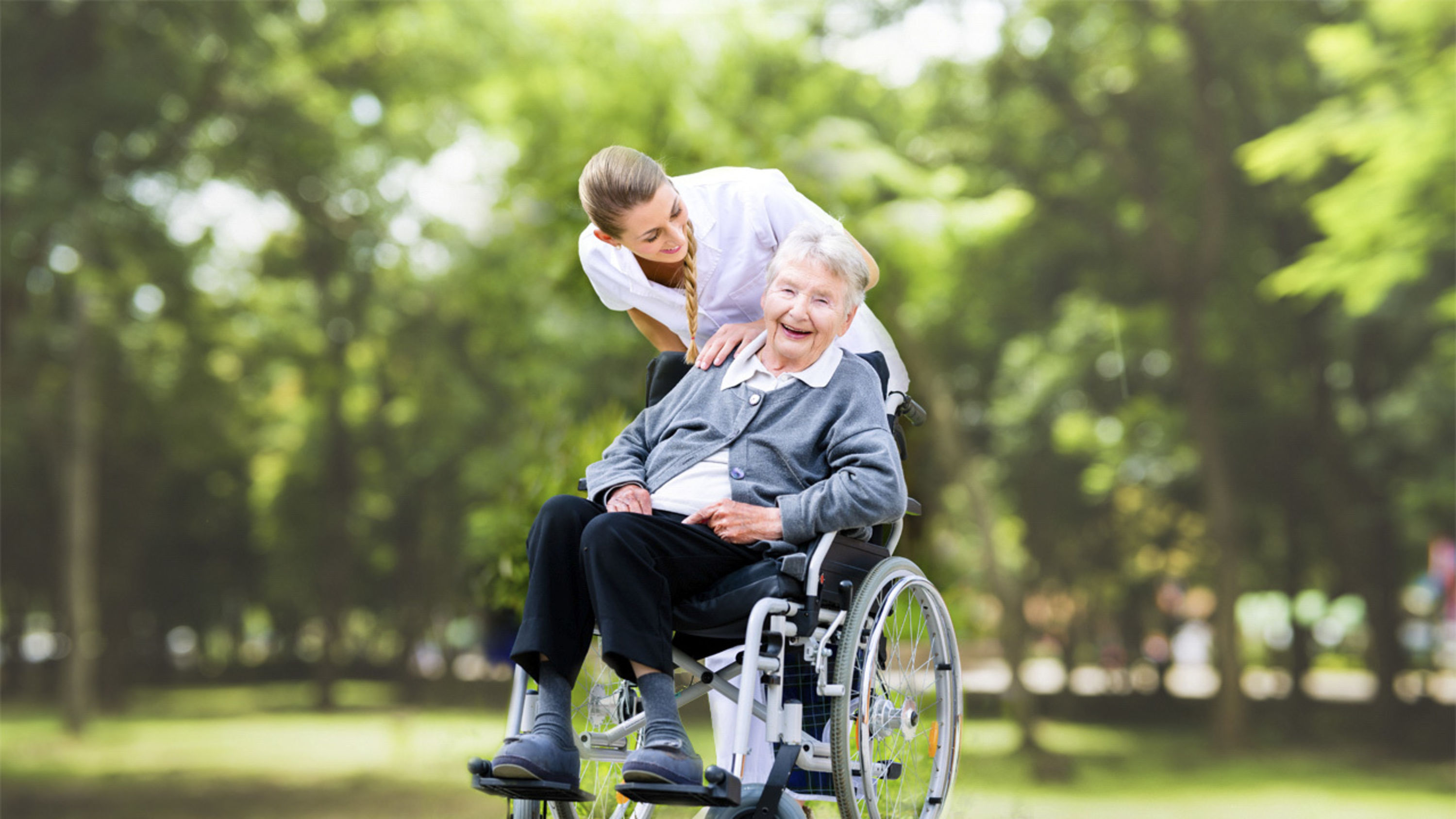 Lachende Pensionistin im Rollstuhl mit Pflegerin.