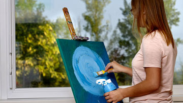Frau malt mit blauer Acrylfarbe auf Leinwand.